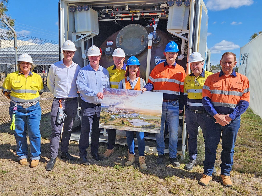 A group of people in business attire and high vis with hardhats stand together and hold a photo of a mock up of a battery project